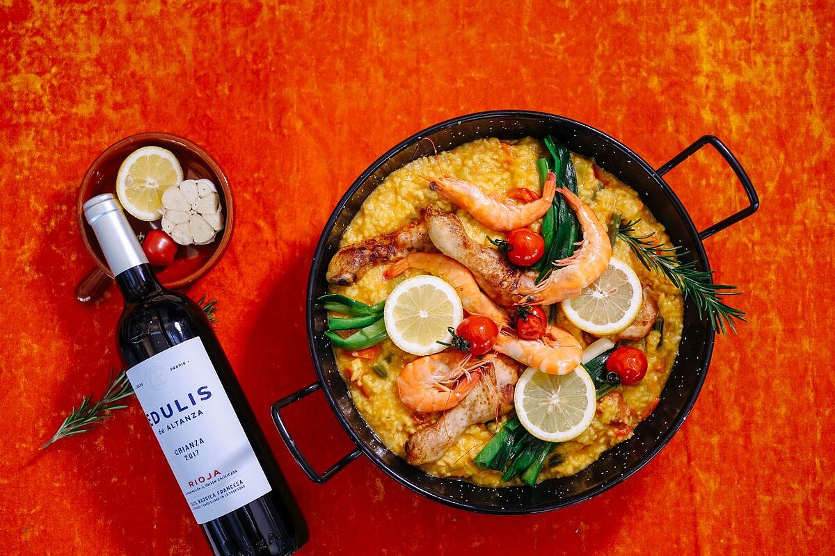 Eine Pfanne voll mit Paella und eine Flasche Wein